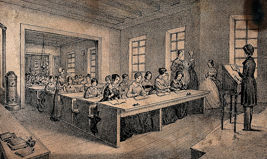 A classroom with children sitting at long tables and a teacher